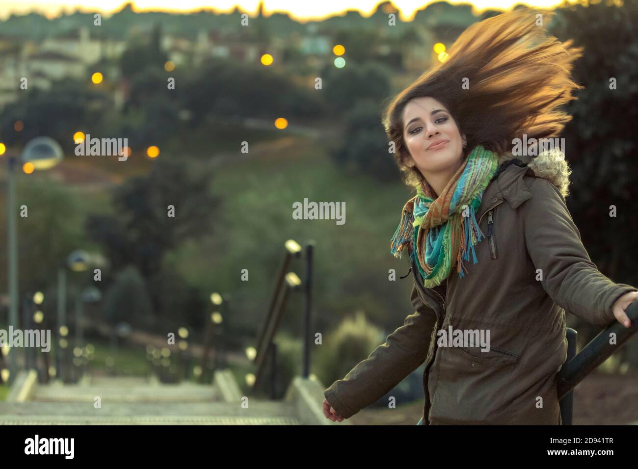 Bella ragazza con cappotto e capelli lunghi nel vento in uno sfondo sfocato Foto Stock