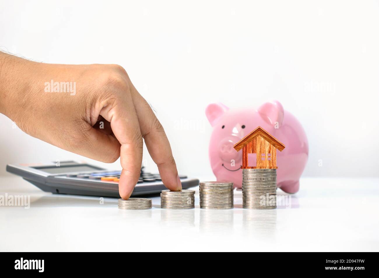 Le mani dell'investitore maschio sono poste sul mucchio di monete, compreso il modello della casa di legno sul mucchio di monete, le idee di risparmio di denaro, la crescita di affari e l'inve Foto Stock