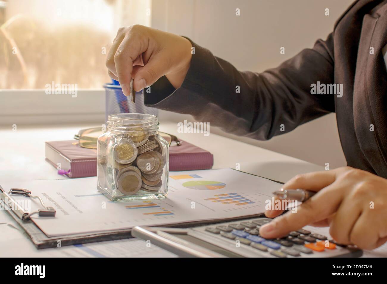 Un uomo d'affari che tiene una moneta in una banca piggy e che preme un concetto finanziario calcolatrice e contabilità finanziaria. Foto Stock