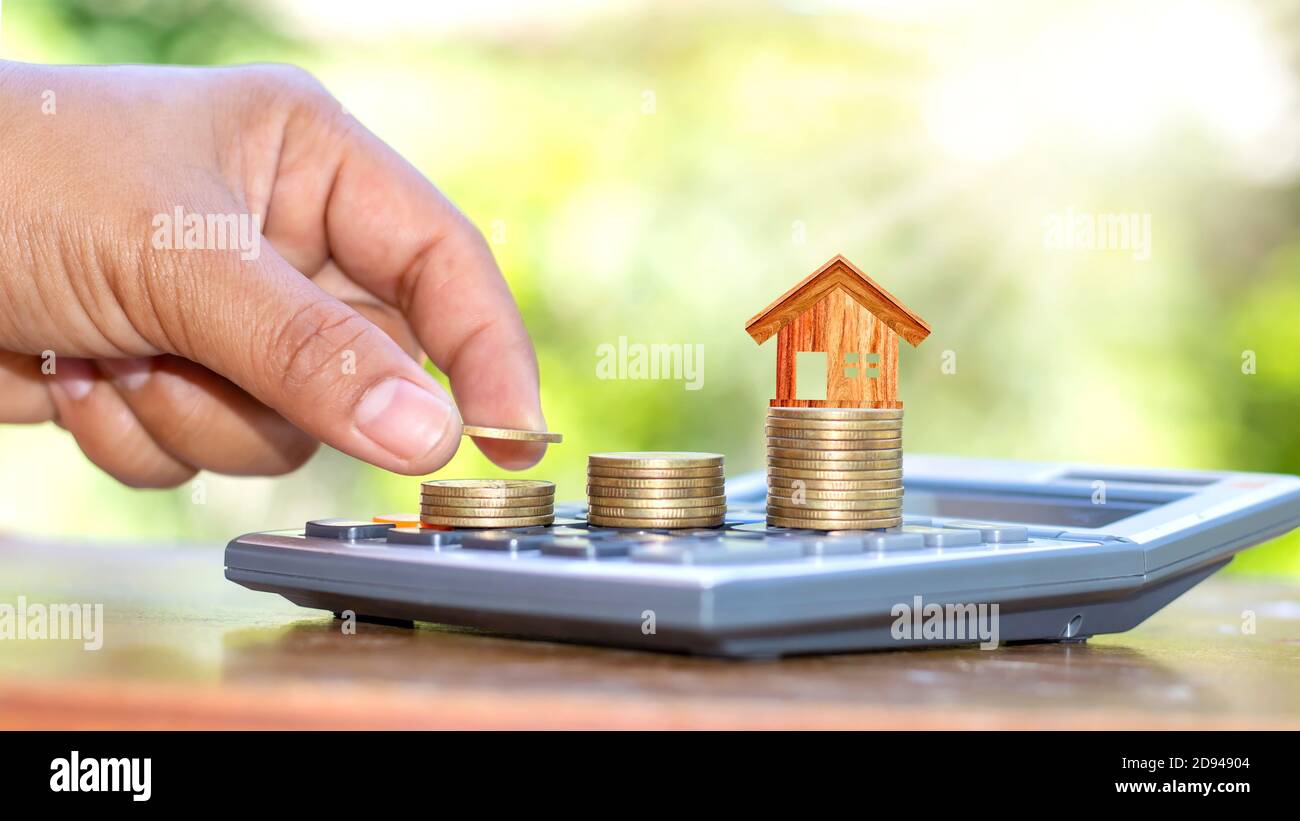 La mano che tiene la moneta e la libera sulla pila di monete include il modello della casa sulla moneta e una calcolatrice. Foto Stock
