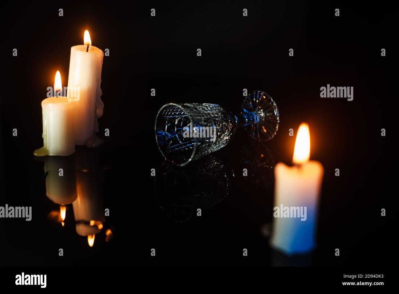 Vetro di cristallo rovesciato che si stende su un tavolo di specchio scuro tra le candele, vista del profilo. Concetto di festa o celebrazione Foto Stock