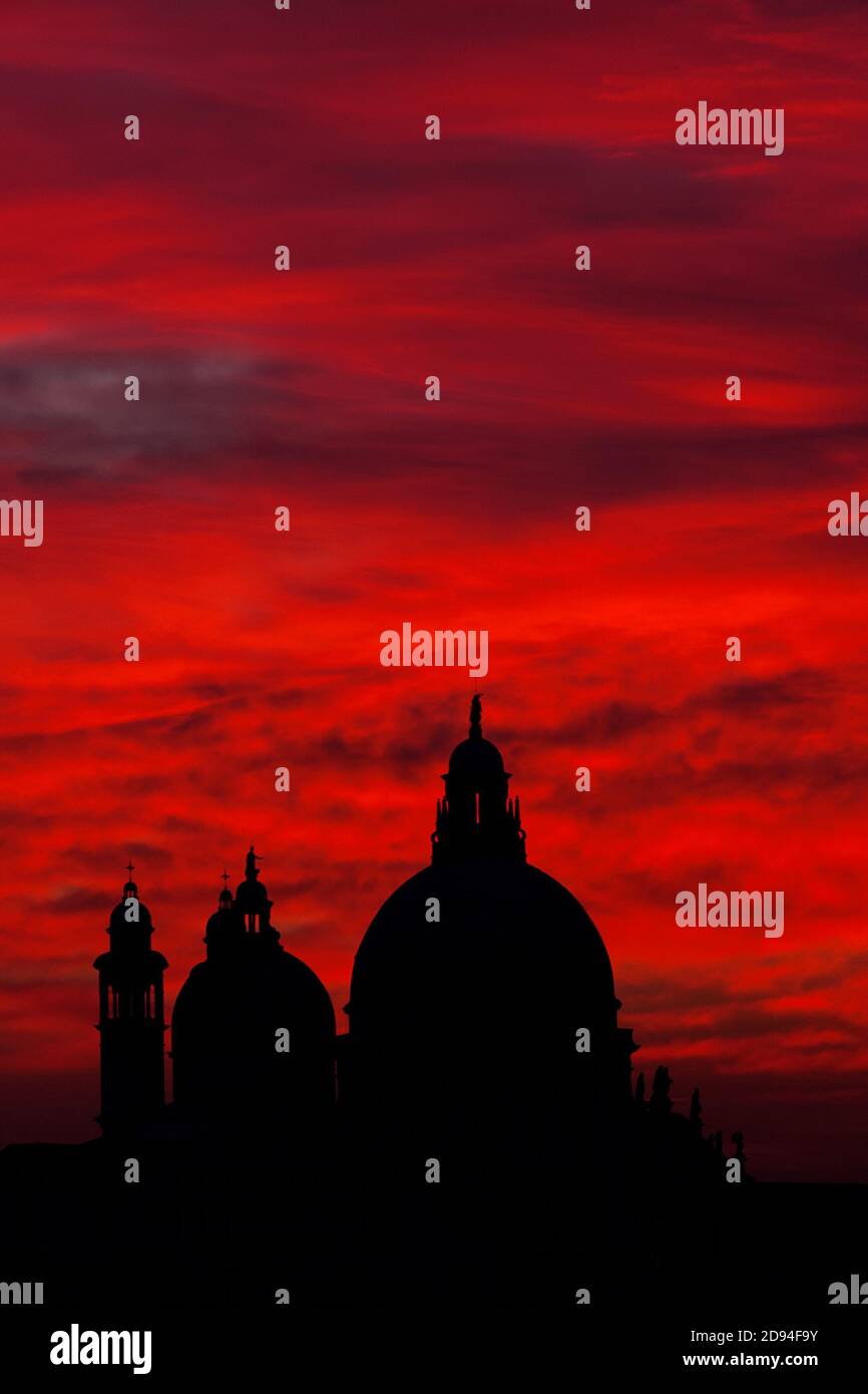 Misterioso cielo rosso tramonto sulla laguna di Venezia con Salute Cupola della Basilica Foto Stock