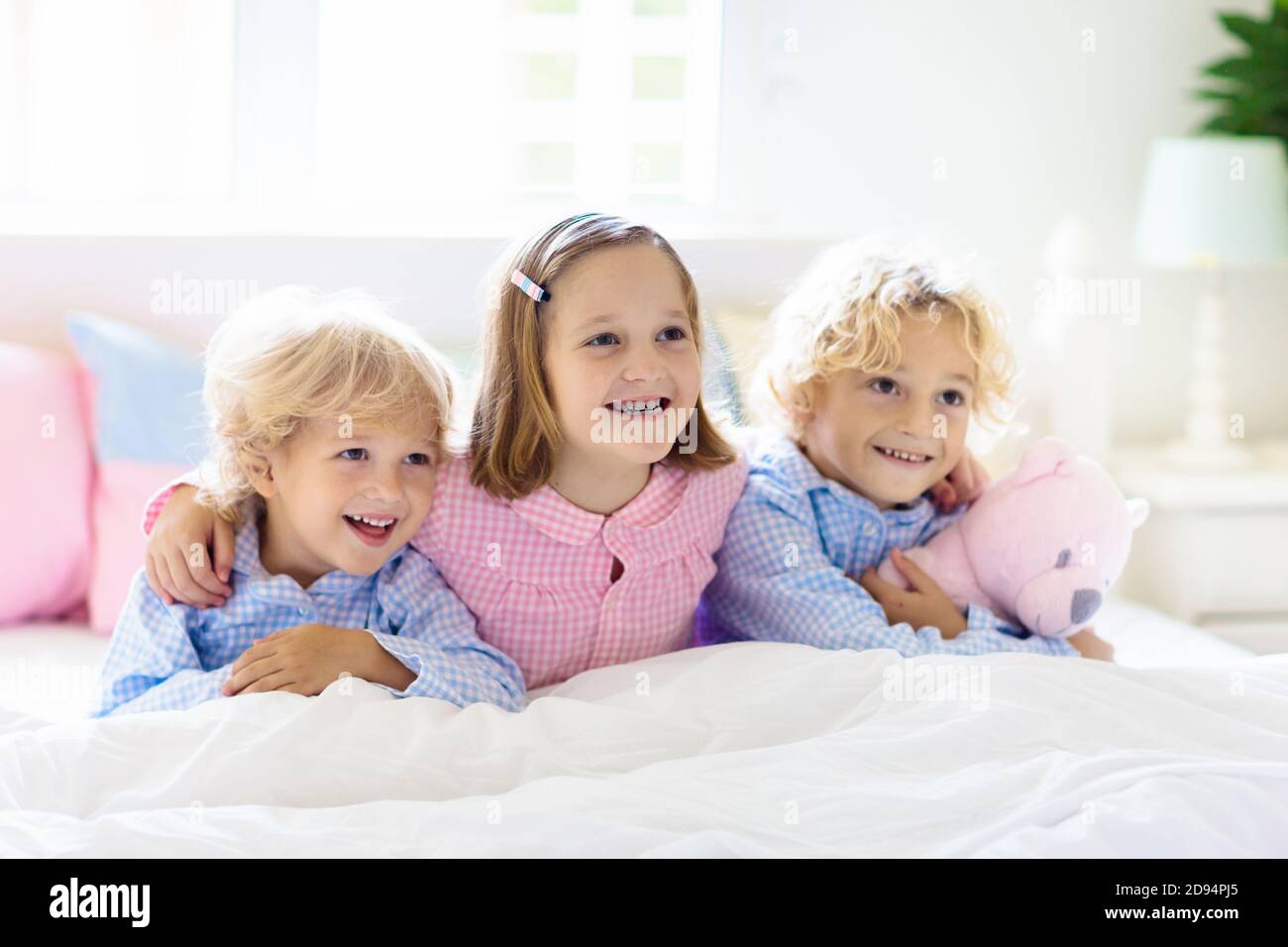 Bambini giocano a letto. I bambini a casa in bianco e luminosa camera da letto. Fratello e Sorella in abbinamento pigiami giocando in camera con i genitori. Mattina in famiglia. Ragazzo e Foto Stock