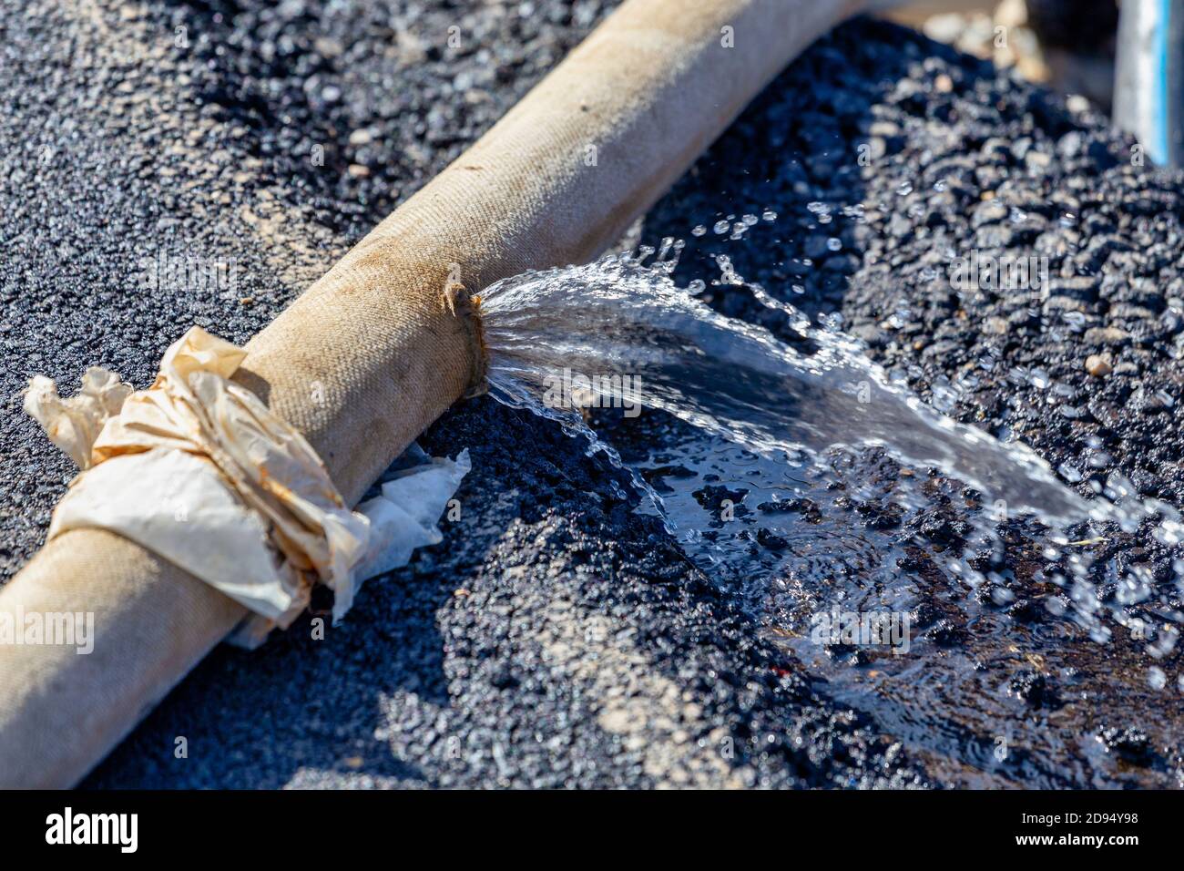 Rottura del tubo flessibile della pompa dell'acqua industriale che perde.  Perdita di acqua dal foro su asfalto Foto stock - Alamy