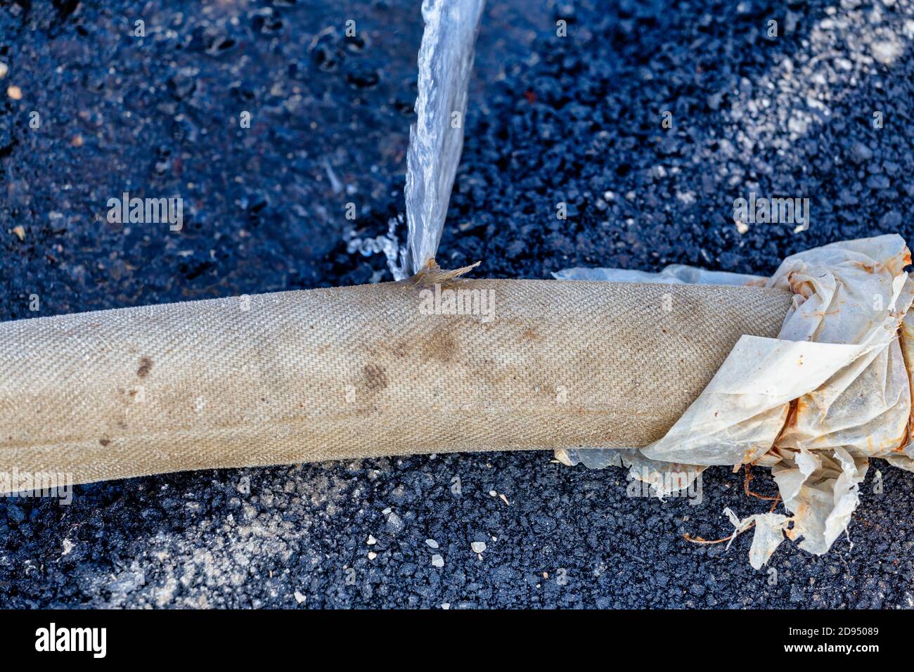Vecchio tubo flessibile rotto che perde della pompa dell'acqua industriale.  Perdita di acqua dal foro su asfalto Foto stock - Alamy