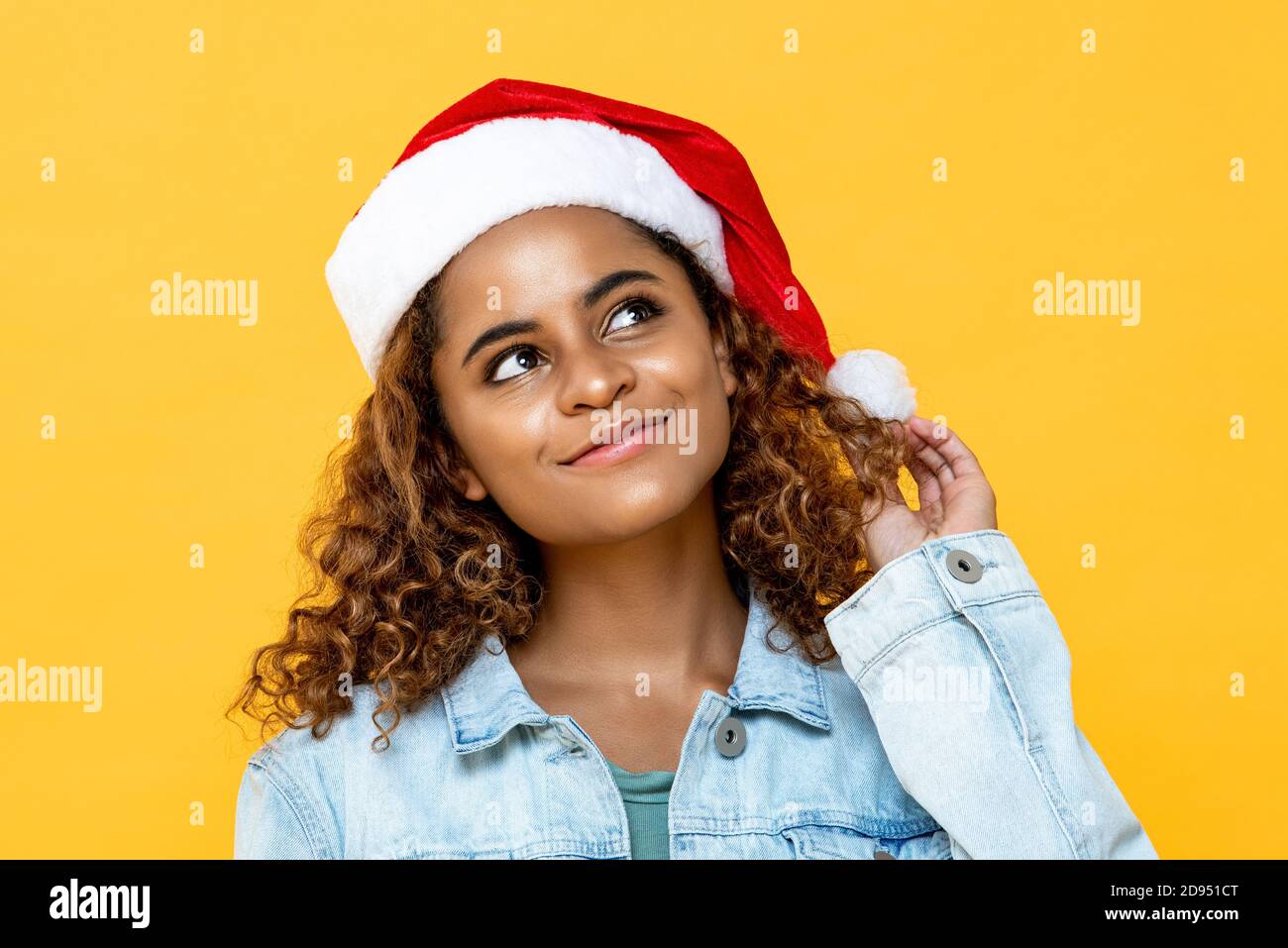 Bella donna afroamericana indossando il cappello di Chritmas sorridente e pensando con gli occhi che guardano fino a spazio da parte isolato su giallo sfondo Foto Stock