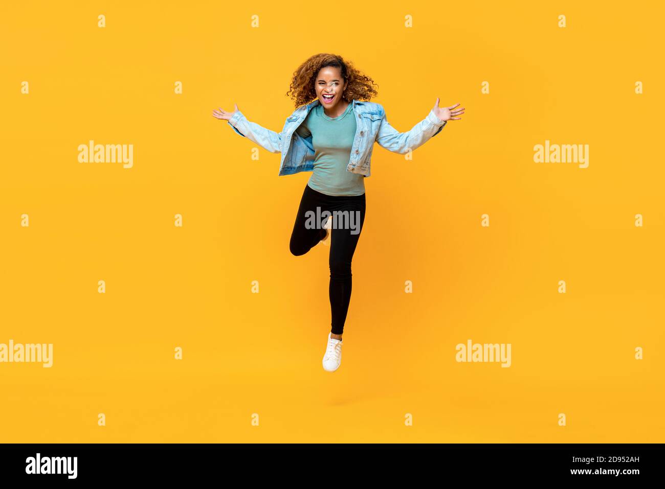 Ritratto a lunghezza intera di giovane energica afroamericana che salta dentro aria media mentre le braccia si allungano in uno studio isolato sfondo giallo Foto Stock