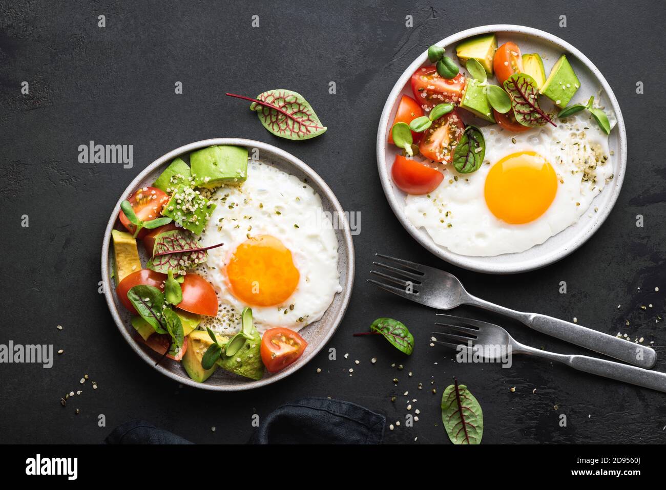 Uova soleggiate con insalata di pomodoro all'avocado. Colazione salutare servita, fondo nero in cemento, vista dall'alto Foto Stock