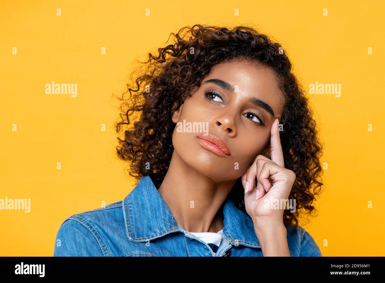Primo piano ritratto di seria giovane donna afroamericana pensare con il dito indice a contatto con la testa in uno sfondo giallo isolato studio Foto Stock