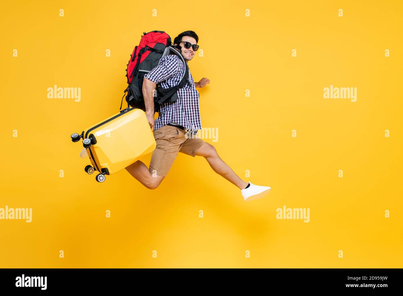 Ritratto di viaggio di giovane eccitata turista caucasica maschile con bagaglio salto in aria media in uno studio isolato sfondo giallo Foto Stock