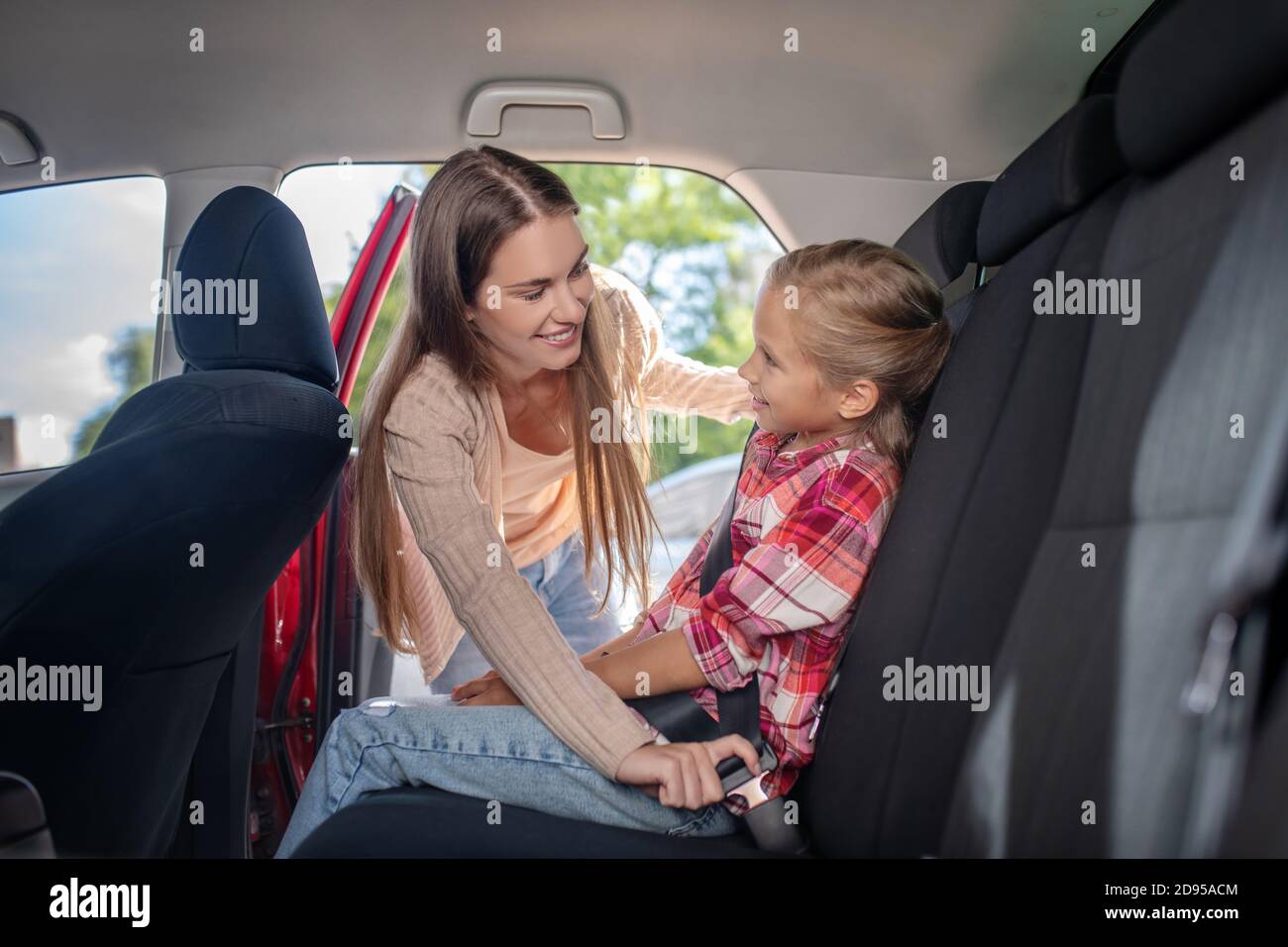 Mamma sorridente allacciando la cintura di sicurezza di sua figlia sul sedile posteriore di auto Foto Stock