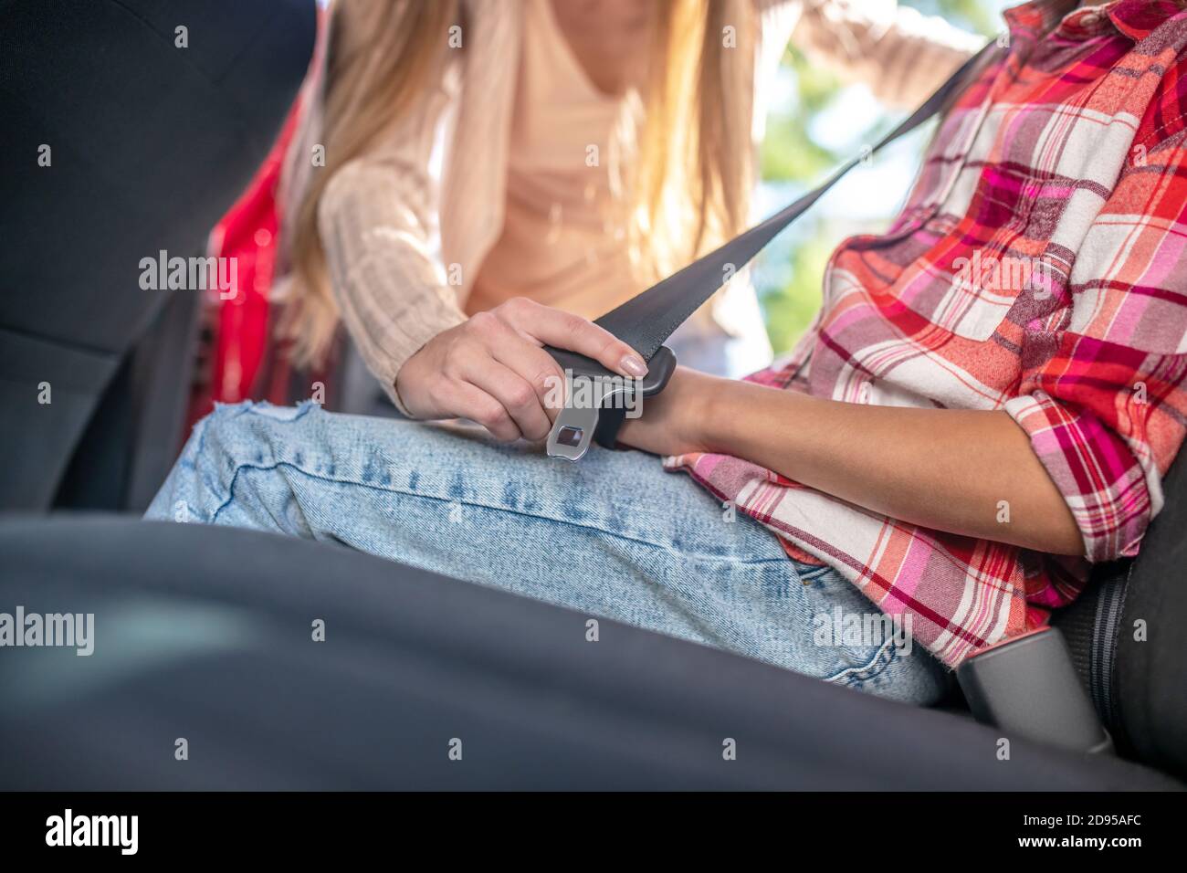 Primo piano delle mani femminili che allacciano la cintura di sicurezza della ragazza sullo schienale di auto Foto Stock