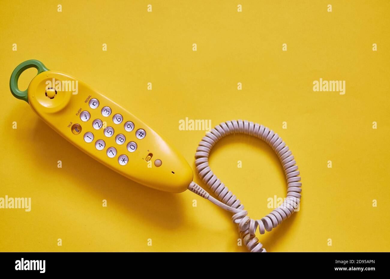 Un ricevitore telefonico giallo con un filo si trova su uno sfondo giallo. La vista dall'alto. Spazio per il testo Foto Stock