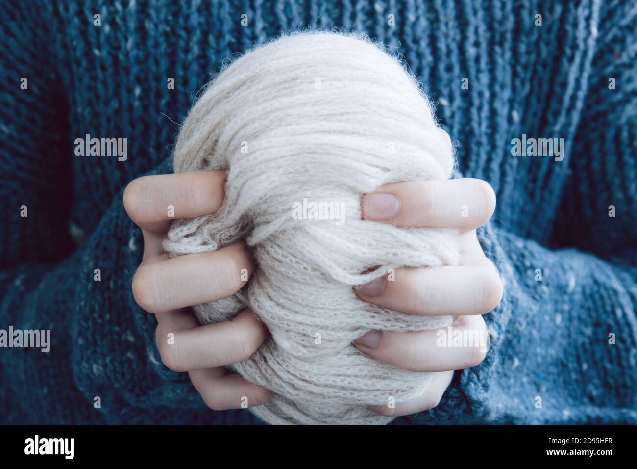 Ragazza in un intimo pullover lavorato a maglia blu scuro tiene dentro mani filo morbido colorato chiaro avvolto in una matassa Foto Stock