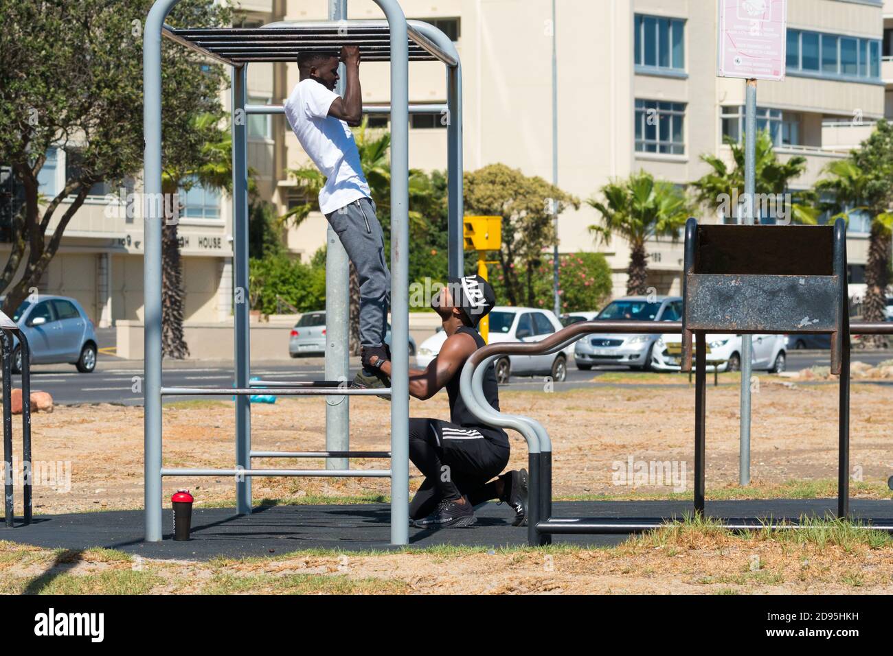 Due uomini neri africani, partner di palestra, allenarsi all'aperto o all'aperto su un apparecchio di palestra facendo bicep tirare insieme concetto di salute e fitness Foto Stock