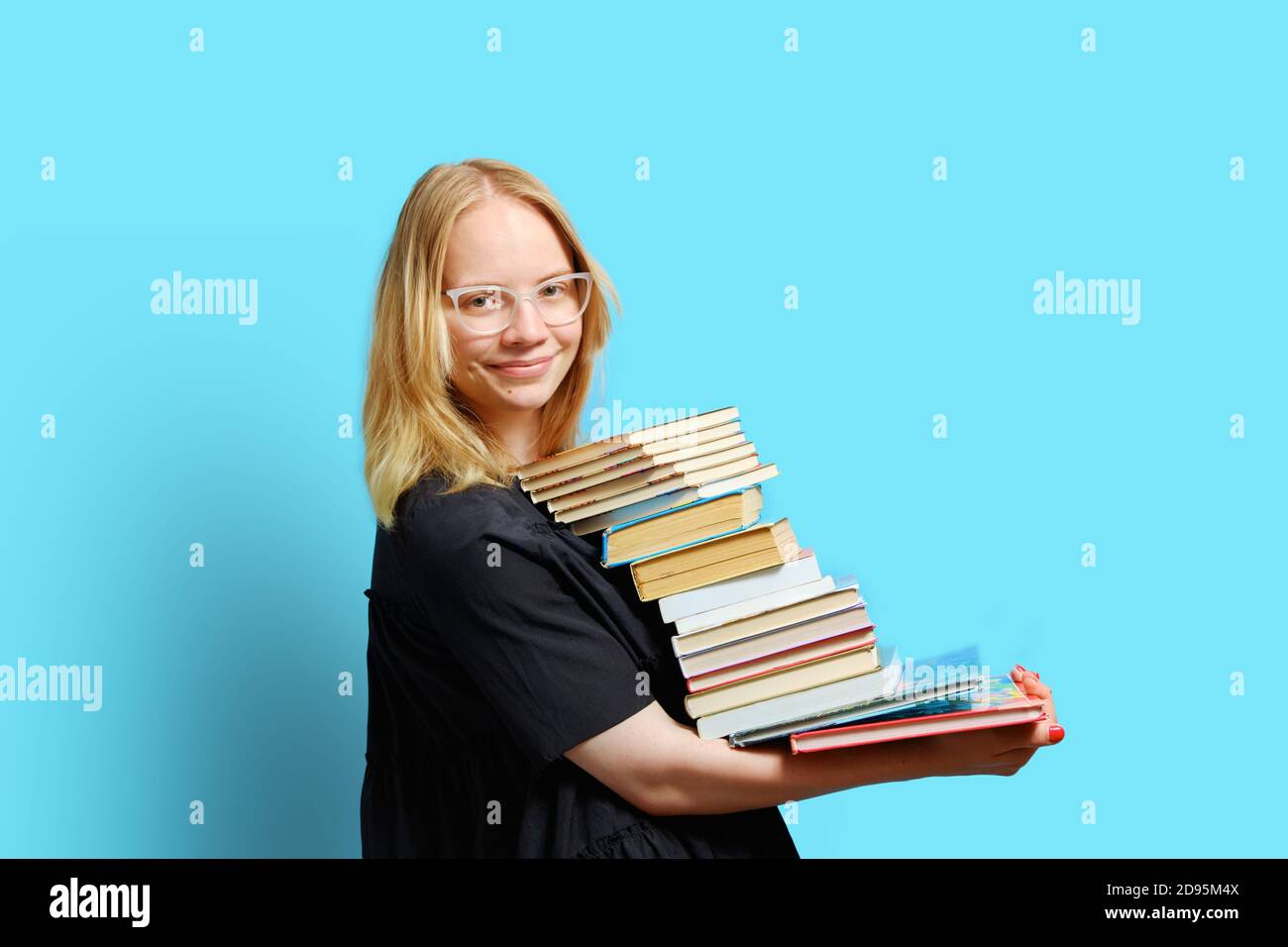 Studio ritratto a mezza lunghezza di un gioioso studente caucasico con una grande pila di libri in mano. Foto Stock