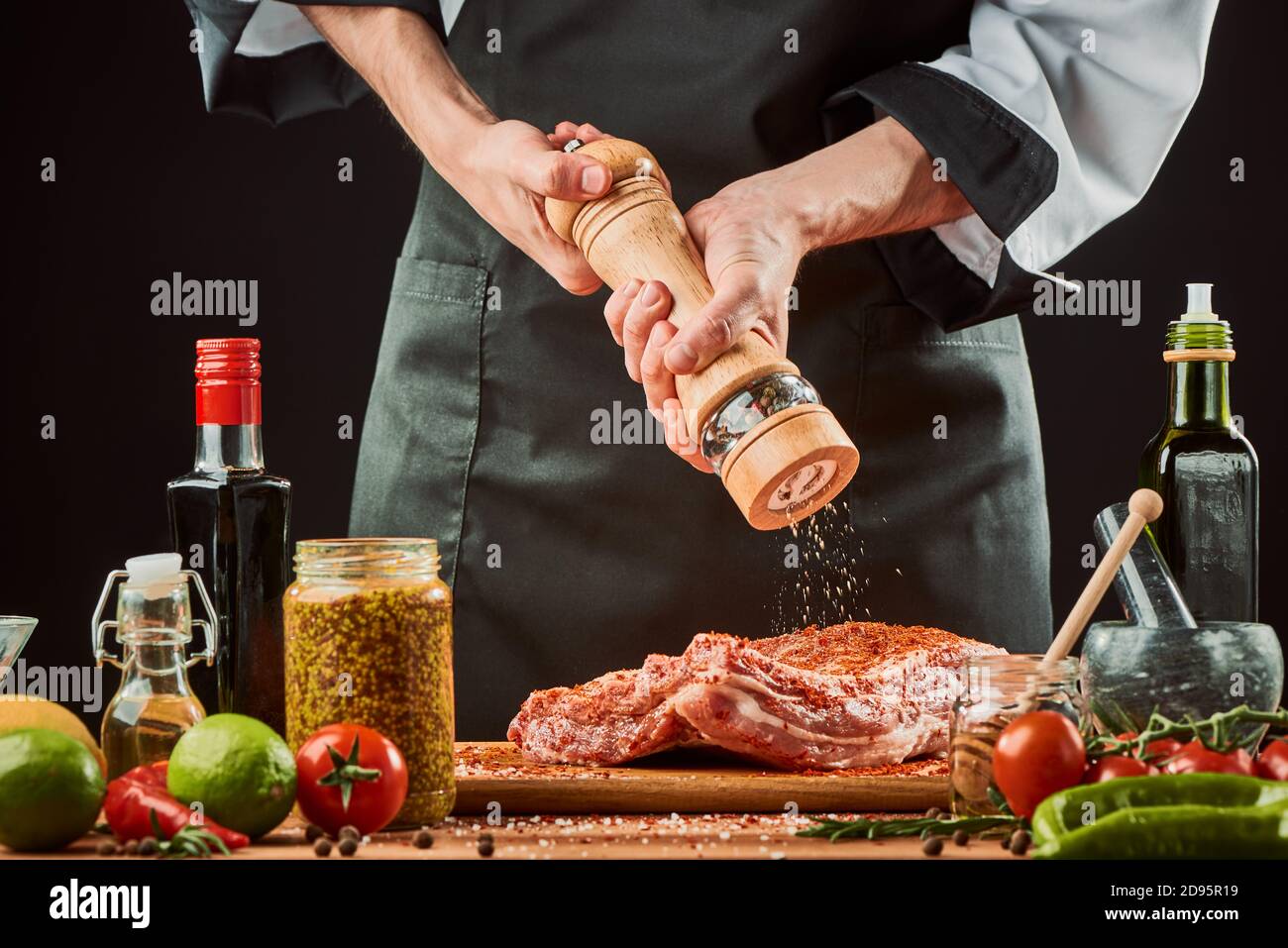 Chef macinando il pepe sulle costolette di manzo. Cuoco professionale condire carne cruda Foto Stock