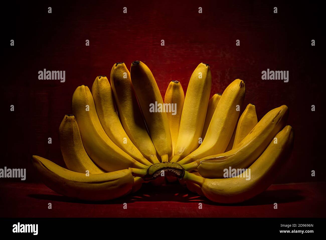 Mazzo di banane giallo maturate su sfondo di legno rosso scuro. Concetto erotico. Foto Stock