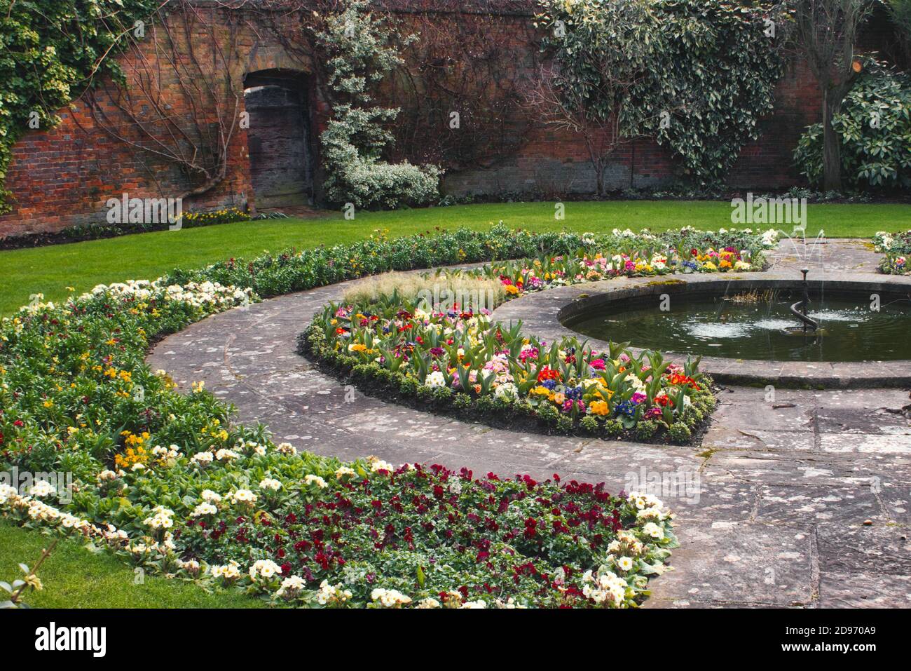 Bellissimo giardino inglese di campagna con aiuole fiorite, un muro circostante e un percorso in pietra con fontana Foto Stock