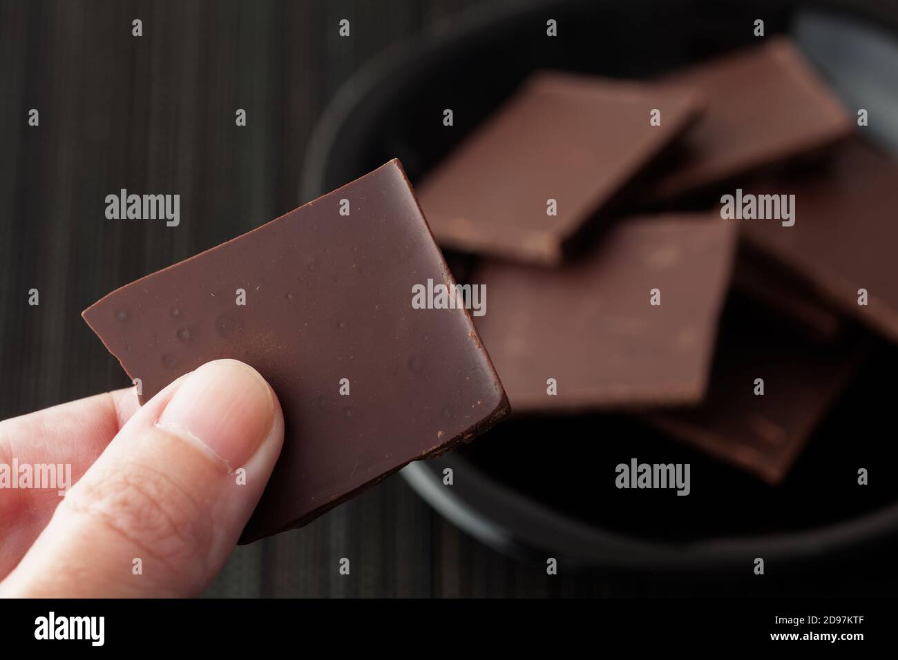 Uomo che tiene un pezzo di cioccolato fondente rotto. Tasto basso. Foto Stock