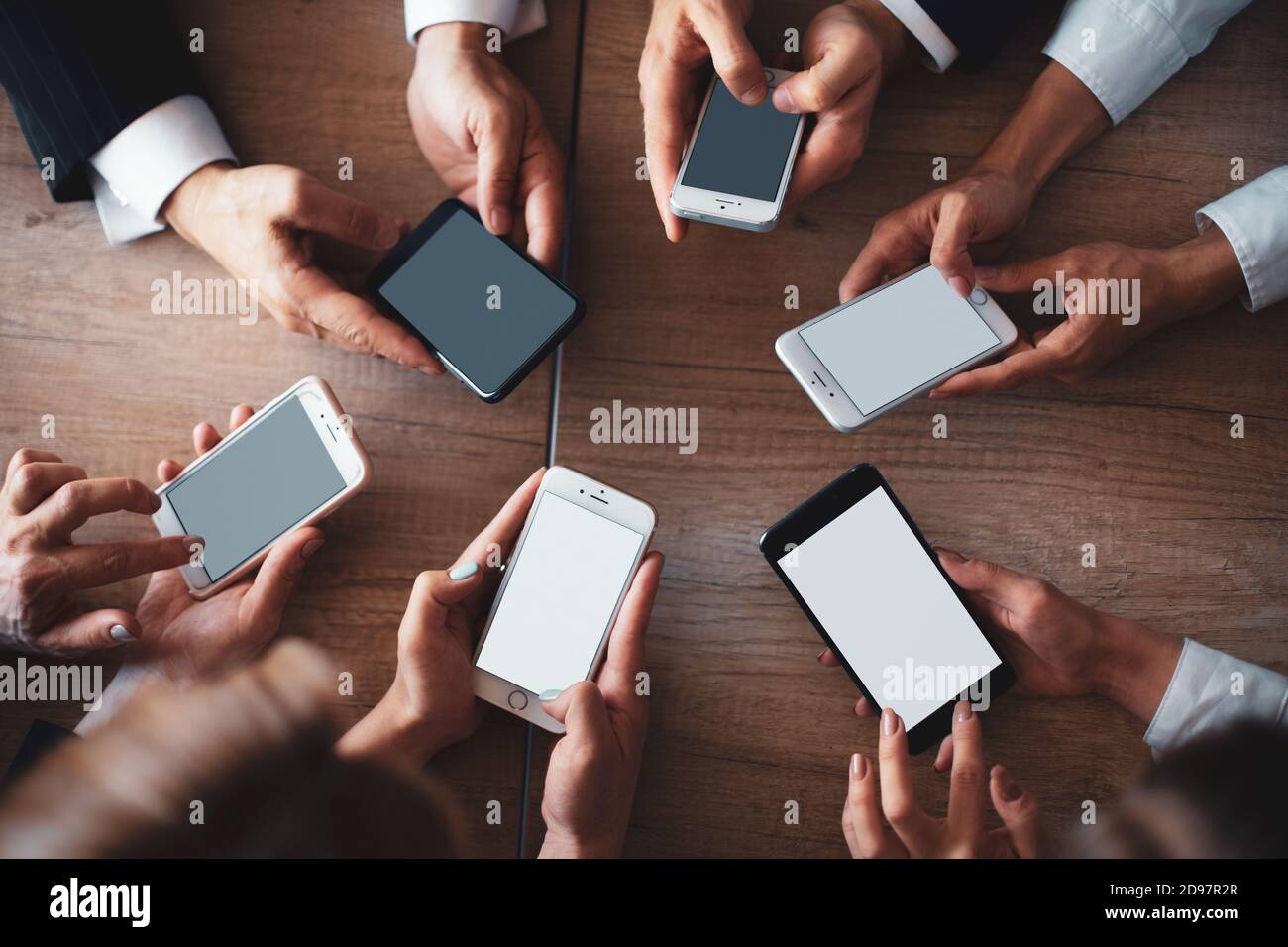 Gli impiegati lavorano sui telefoni. Concetto di riunione mobile. Primo piano delle mani umane utilizzando gli smartphone su un tavolo di legno. Vista dall'alto Foto Stock