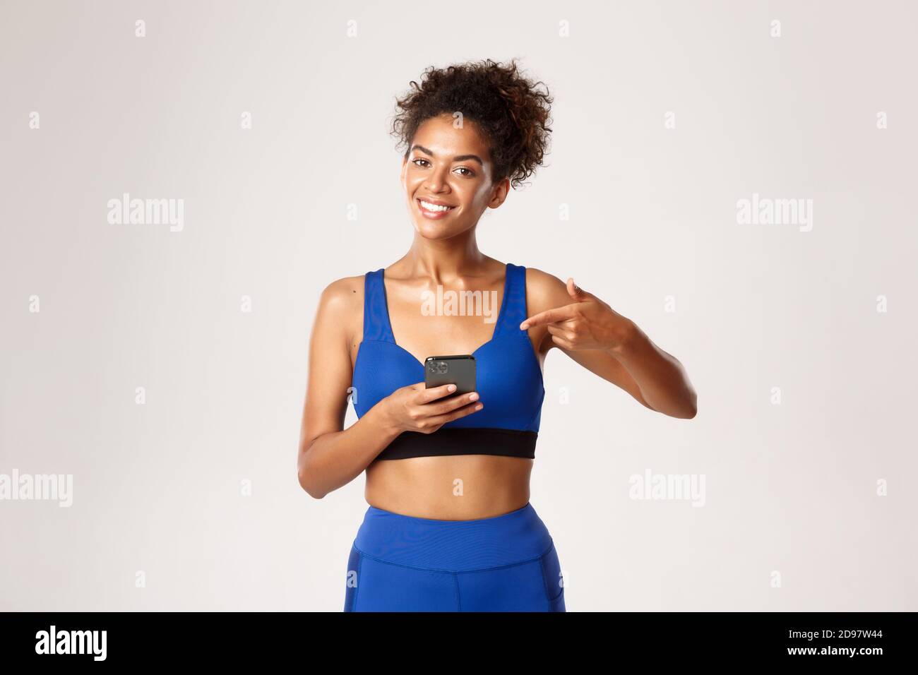 Concetto di sport e tecnologia. Attraente donna afroamericana di idoneità in sport, puntando il dito al telefono mobile, consiglia l'applicazione di allenamento Foto Stock