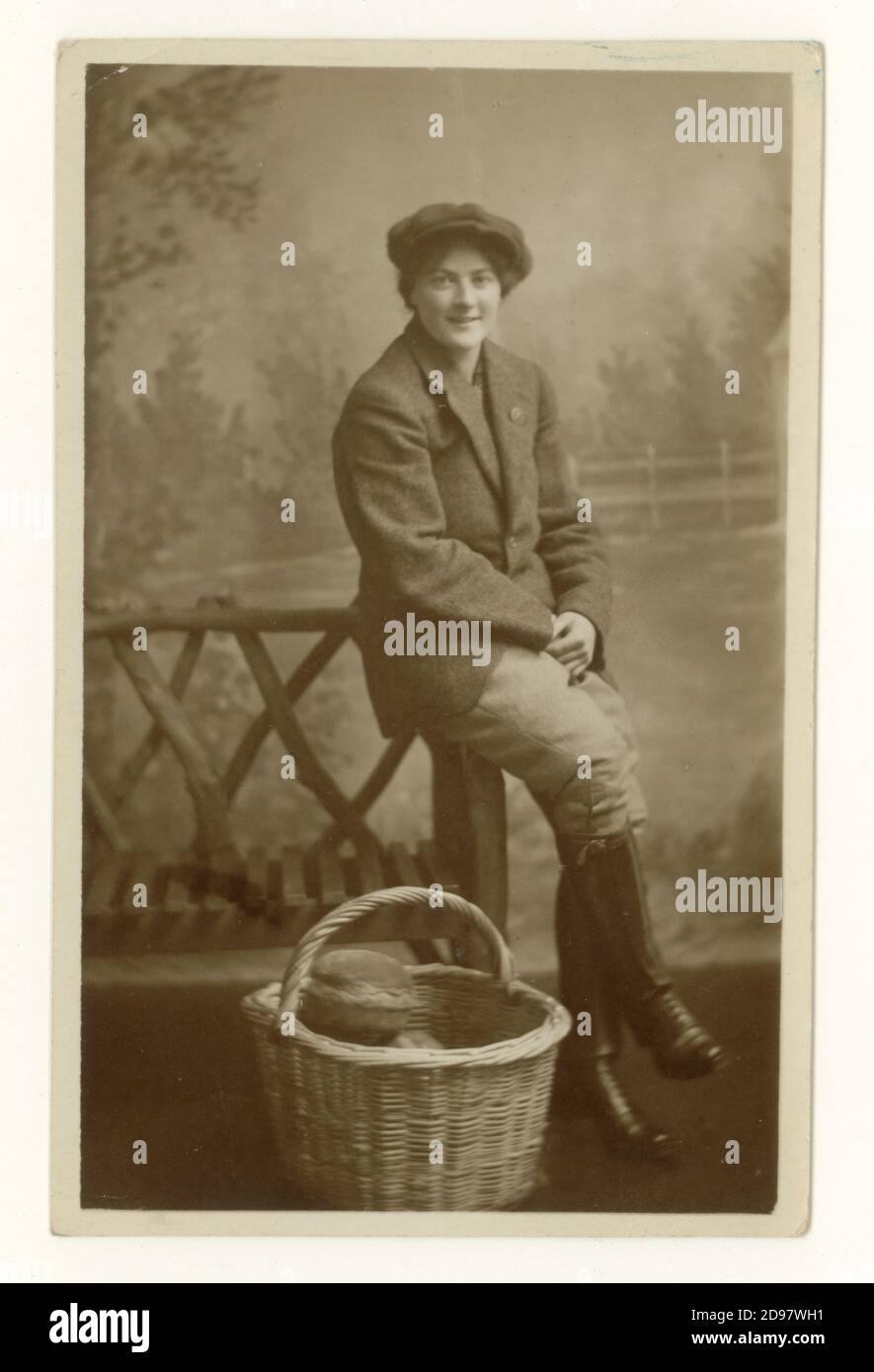 Originale cartolina studio dell'era WW1 di attraente Land Girl nella Women's Land Army (WLA) - indossando braghe, giacca e cappello con un cestino di pane pagnotte, coinvolto nella raccolta del grano, sezione agricola della WLA, datata agosto 1918 sul retro, Regno Unito Foto Stock