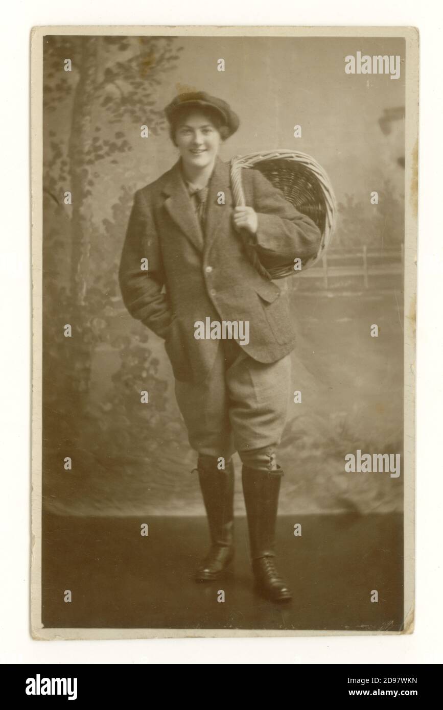 Originale cartolina studio dell'era WW1 di attraente Land Girl nella Women's Land Army (WLA) indossando braghe, giacca e cappello che reggono un cestino di pane, coinvolto nella raccolta del grano, sezione agricola della WLA, datata agosto 1918 sul retro, Regno Unito Foto Stock