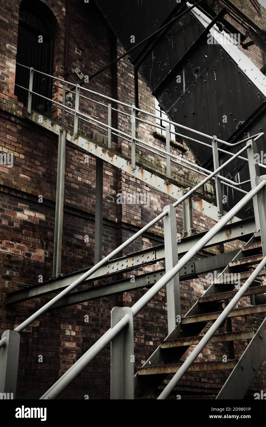 Vecchie scale in acciaio arrugginito all'esterno dell'edificio industriale in mattoni,. Foto Stock