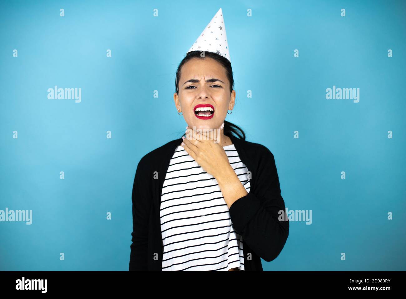 Giovane bella donna che indossa un cappello di compleanno su sfondo blu insolato toccando collo doloroso, mal di gola per influenza, coagulo e infezione Foto Stock
