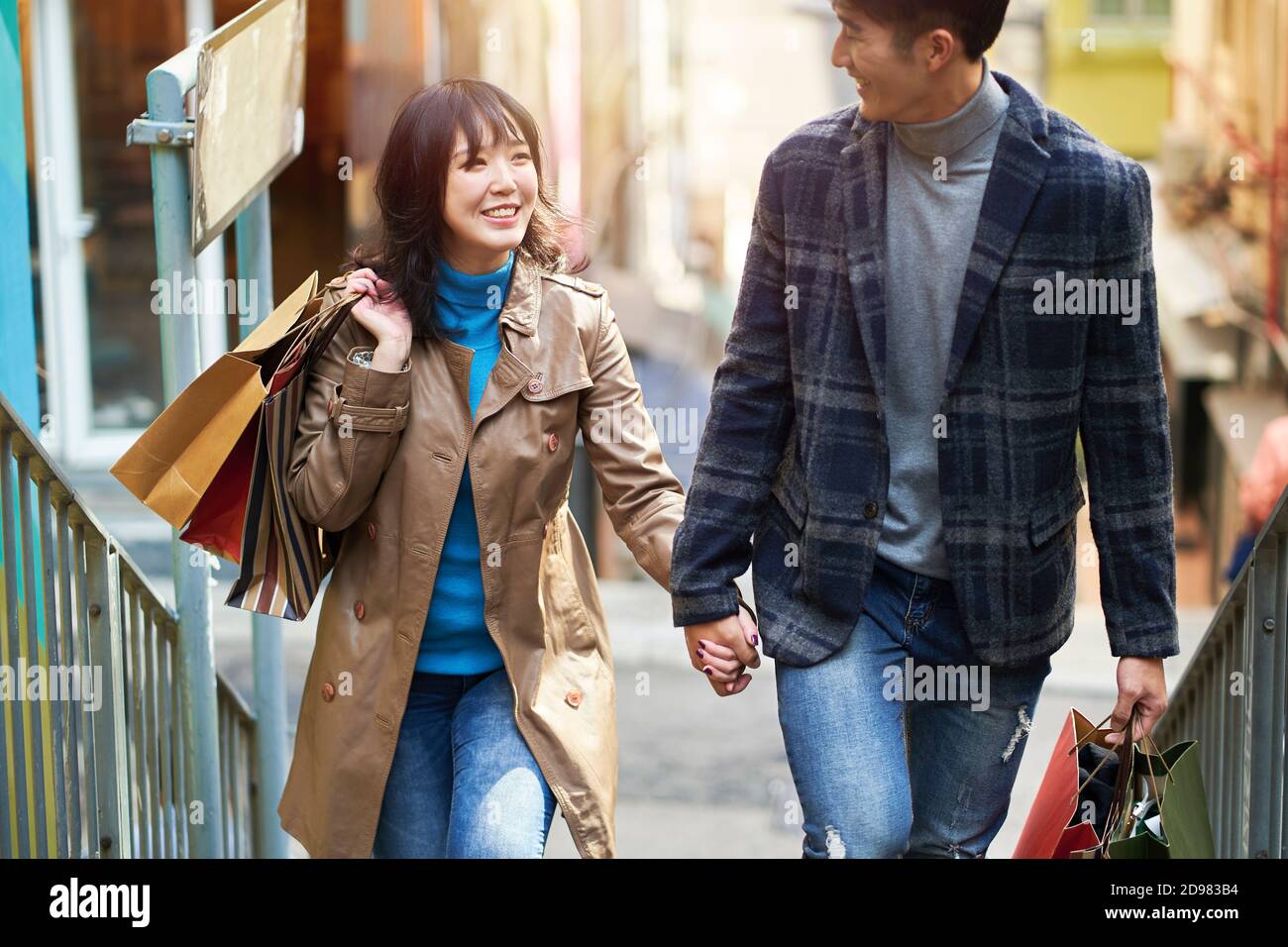 felice giovane coppia asiatica che cammina parlando tenendo le mani mentre si fa shopping in città Foto Stock