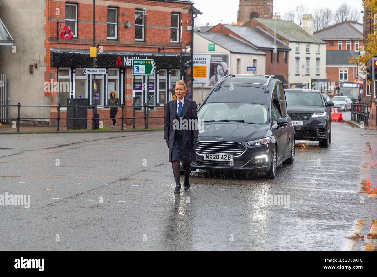 Il corteo funebre viaggia lentamente attraverso un villaggio con una femmina direttore funebre che cammina di fronte Foto Stock