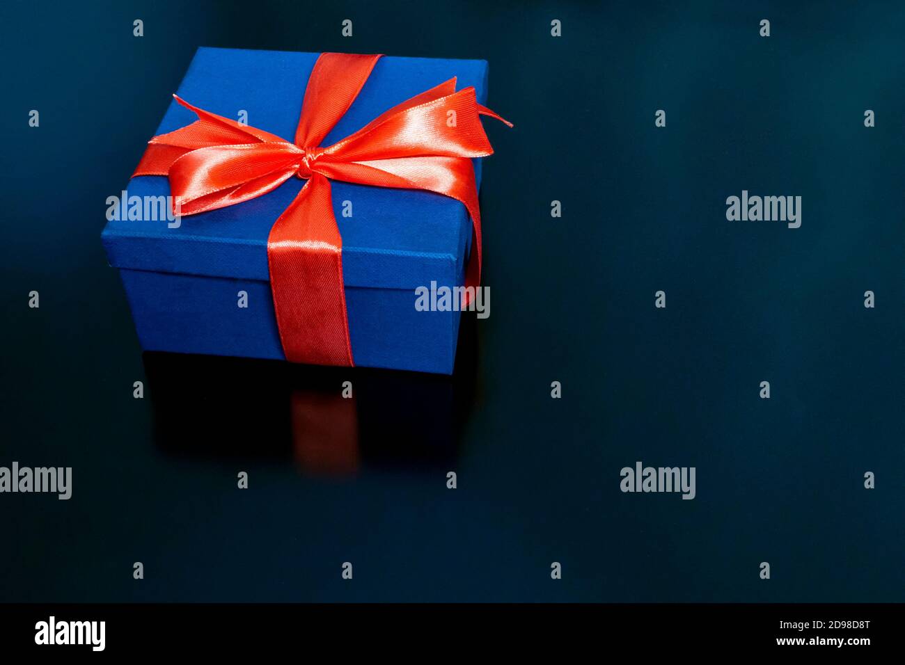 su uno sfondo nero è una scatola regalo blu scuro legato con un nastro rosso Foto Stock