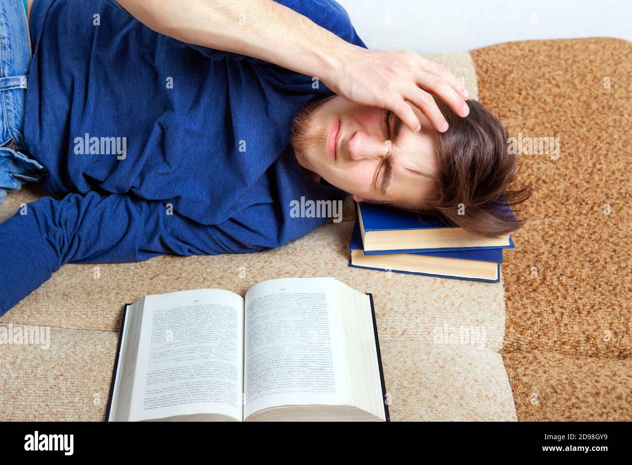 Sleepy e stanco giovane uomo sul divano con un Prenota Foto Stock