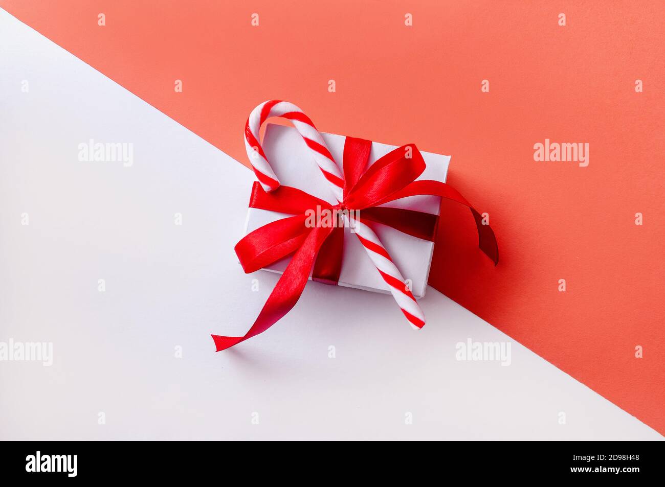 Confezione regalo di Natale su sfondo rosa e bianco con caramella. Composizione minima creativa Foto Stock