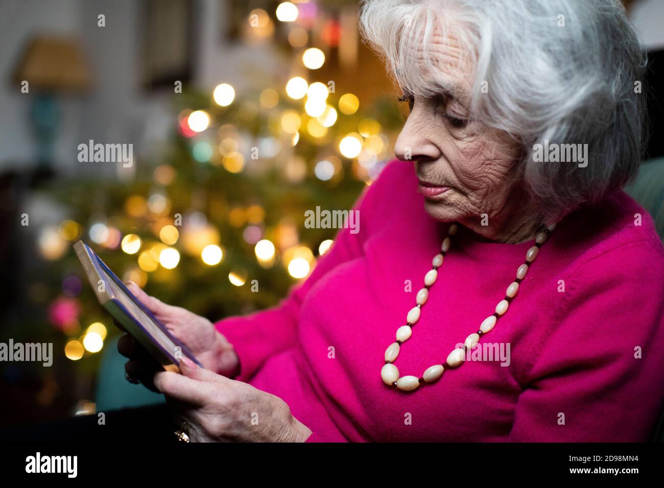 Donna triste e Lonely Senior che passa Natale a casa da sola Guardando la fotografia di famiglia Foto Stock