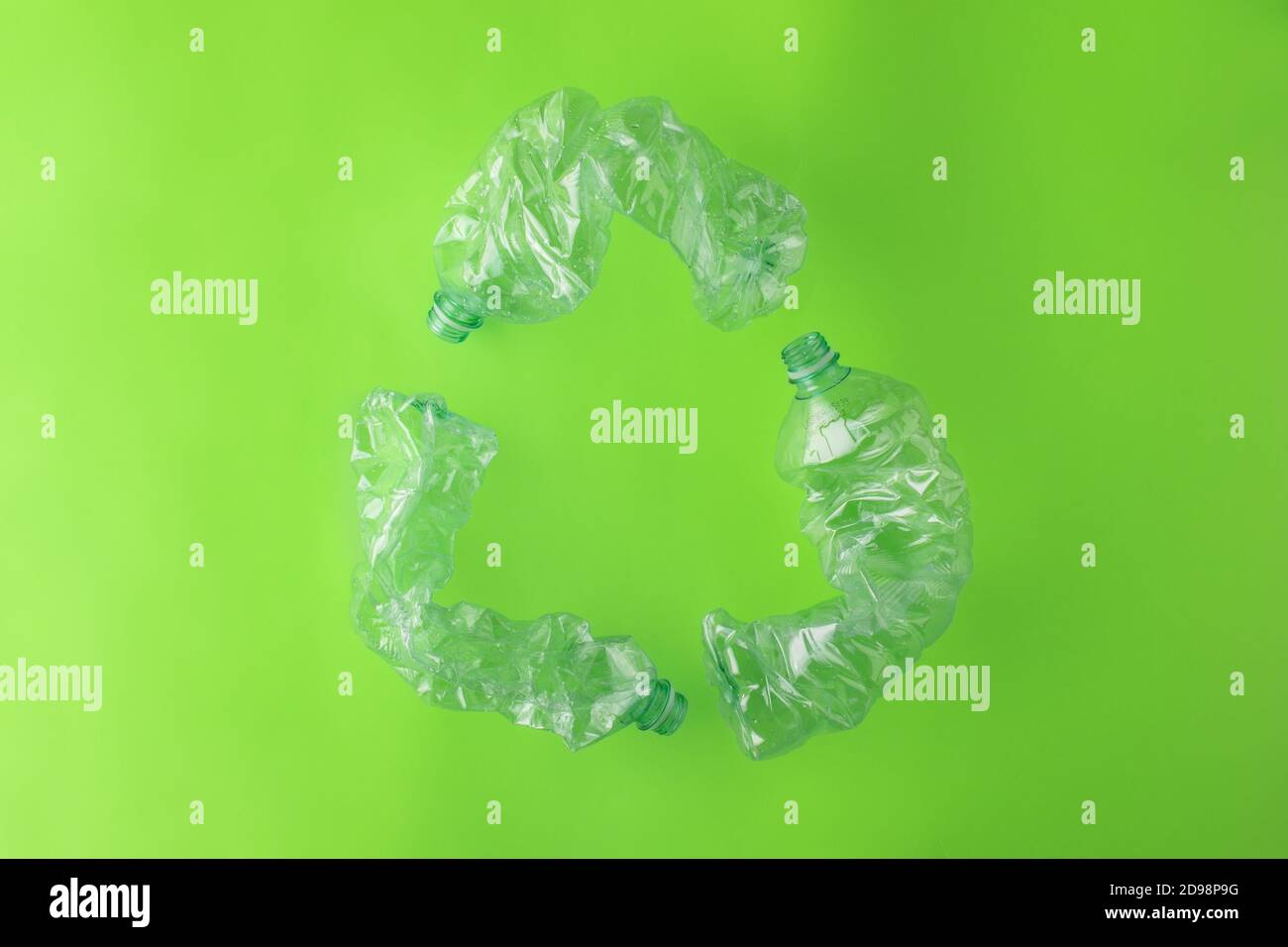 Simbolo di riciclaggio realizzato con tre bottiglie di plastica su sfondo verde Foto Stock