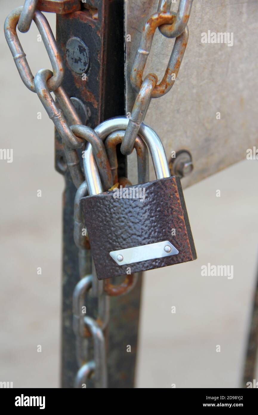 Un nuovo lucchetto marrone ad arco lucido è appeso su una catena su una porta in ferro. Foto Stock