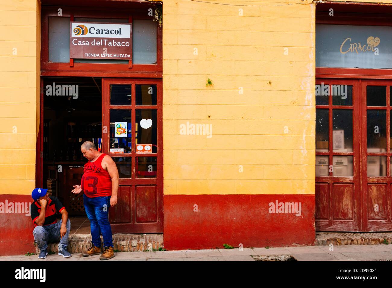 Due uomini cubani parlano all'ingresso di una tabaccheria cubana di stato. Trinidad, Sancti Spíritus, Cuba, America Latina e Caraibi Foto Stock