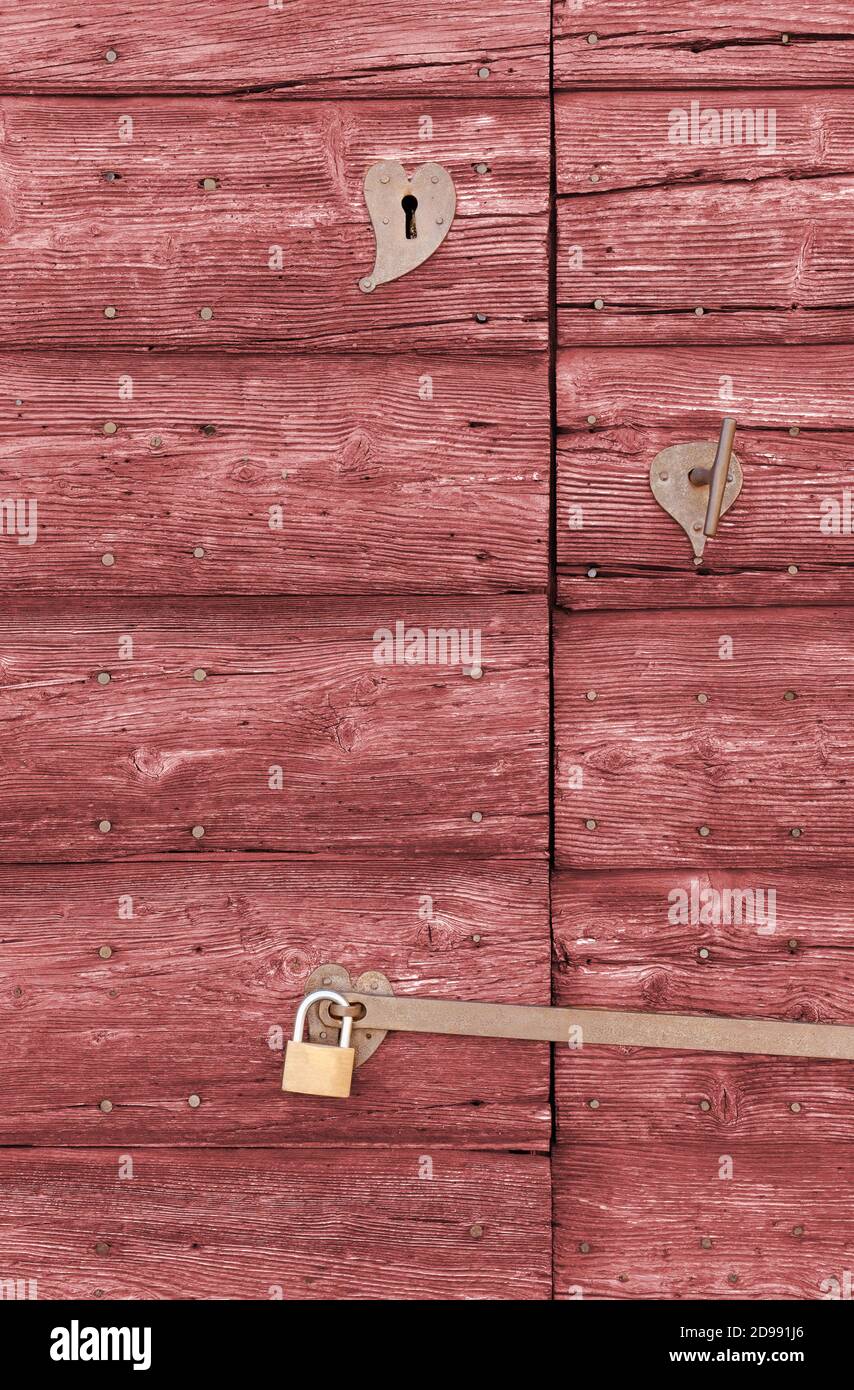 Primo piano di una vecchia porta esterna in legno di colore rosso con un impugnatura in ferro e due serrature Foto Stock