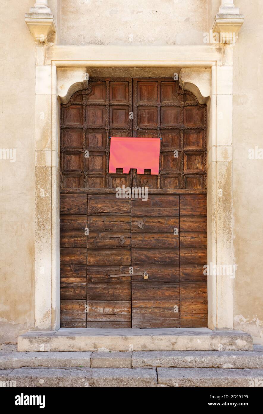 Antico portale ligneo di un'antica chiesa, con una vuota bandiera rossa appesa su di essa Foto Stock