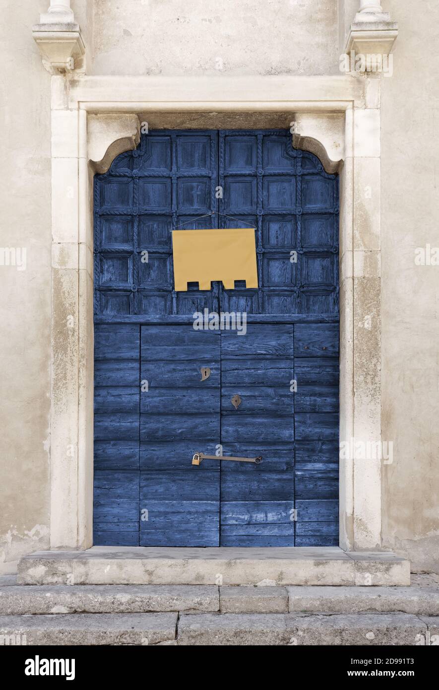Antico portale ligneo di colore blu di un'antica chiesa, con una vuota bandiera gialla appesa su di essa Foto Stock
