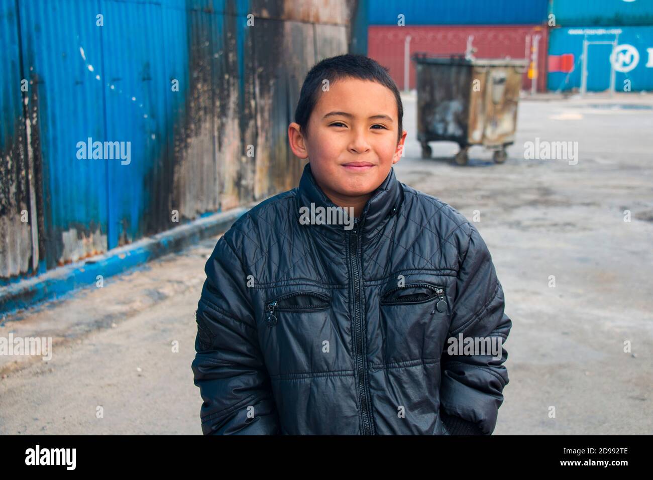 Un bambino sorride con ansia senza sapere cosa regge il futuro. Skaramagas ospita un campo profughi "temporaneo", una sorta di sala d'attesa dove i migranti provenienti principalmente da Siria, Iraq e Afghanistan soggiornano prima di essere reinsediati altrove in Europa. A Skaramagas, possono anche sapere se la loro richiesta di trasferimento è stata approvata o respinta. Makariou, Skaramagkas, Grecia. Foto Stock