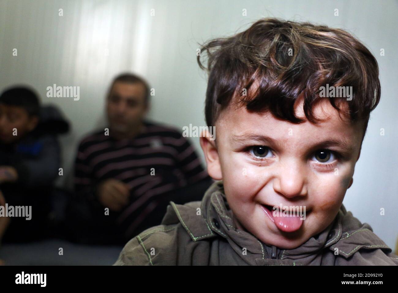 Un bambino sorride con ansia senza sapere cosa regge il futuro. Skaramagas ospita un campo profughi "temporaneo", una sorta di sala d'attesa dove i migranti provenienti principalmente da Siria, Iraq e Afghanistan soggiornano prima di essere reinsediati altrove in Europa. A Skaramagas, possono anche sapere se la loro richiesta di trasferimento è stata approvata o respinta. Makariou, Skaramagkas, Grecia. Foto Stock