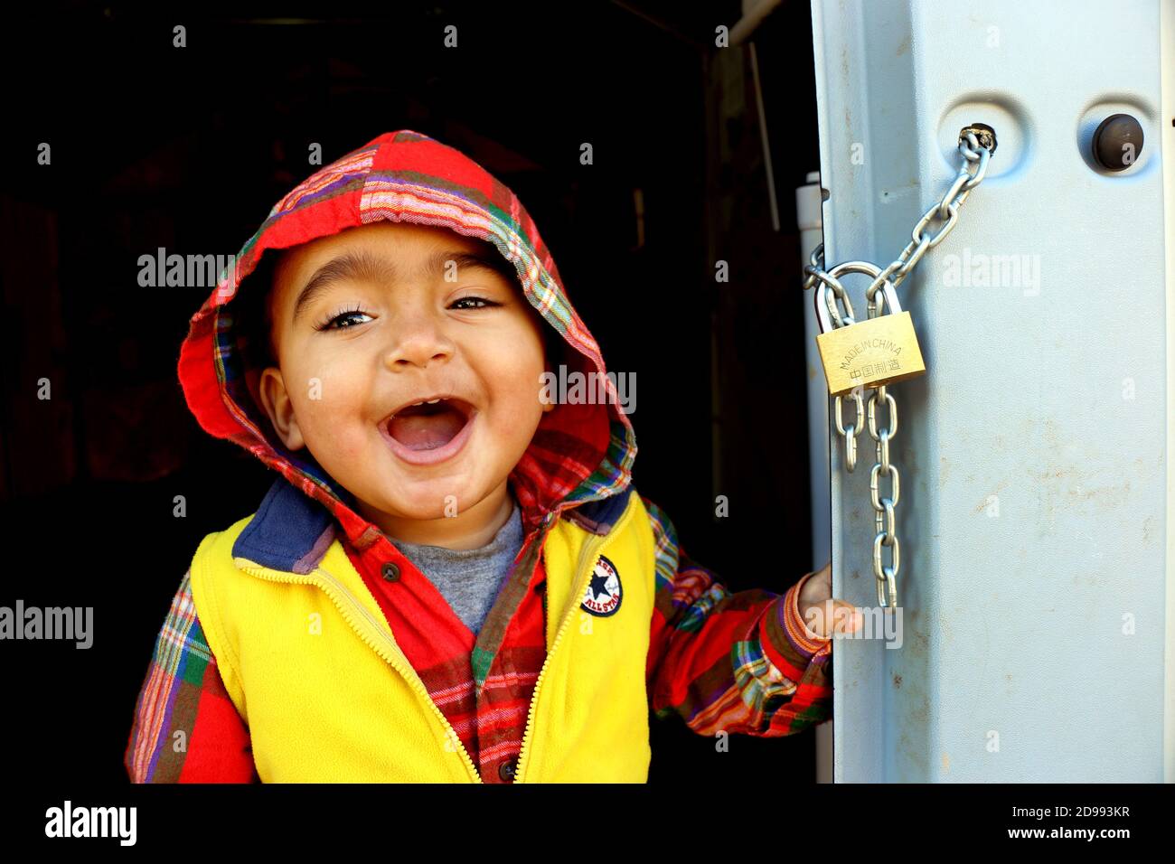 Un bambino sorride con ansia senza sapere cosa regge il futuro. Skaramagas ospita un campo profughi "temporaneo", una sorta di sala d'attesa dove i migranti provenienti principalmente da Siria, Iraq e Afghanistan soggiornano prima di essere reinsediati altrove in Europa. A Skaramagas, possono anche sapere se la loro richiesta di trasferimento è stata approvata o respinta. Makariou, Skaramagkas, Grecia. Foto Stock