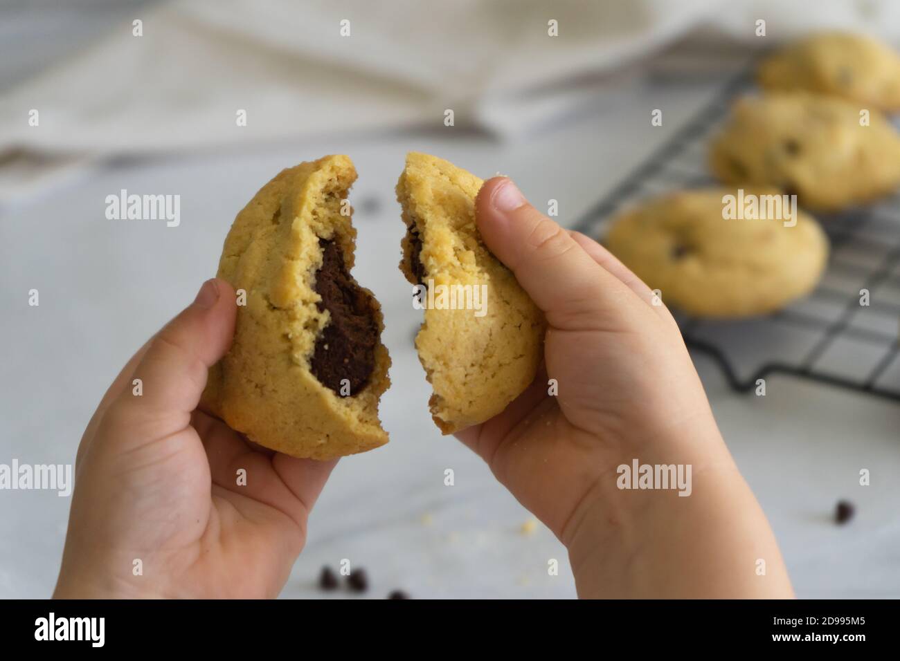 Le mani dei bambini rompono un biscotto di chip di cioccolato su sfondo bianco. Cotto in casa. Foto Stock