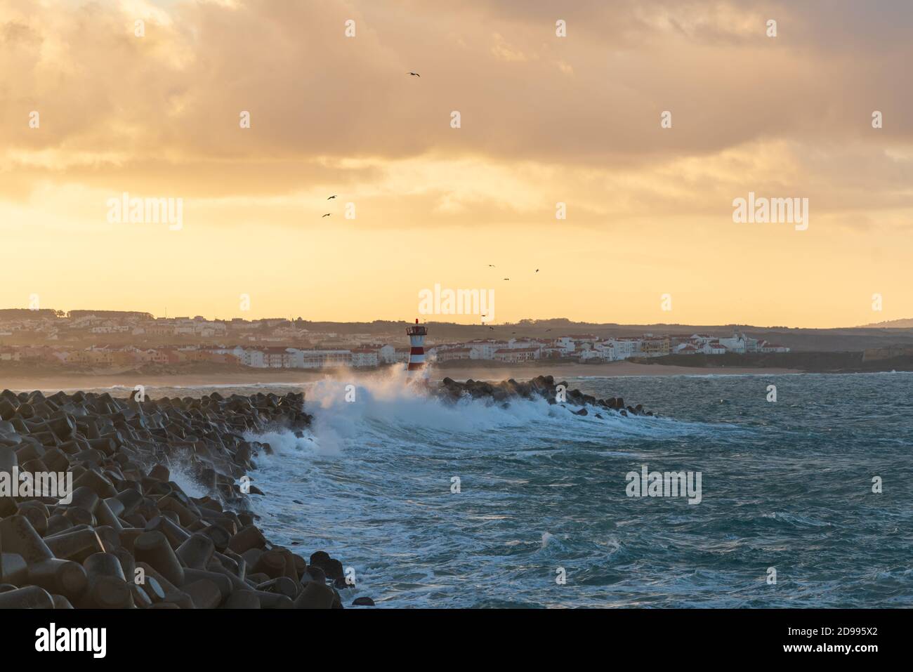 Faro di Peniche con spiaggia di Supertubos sullo sfondo al tramonto con onde che si infrangono, in Portogallo Foto Stock