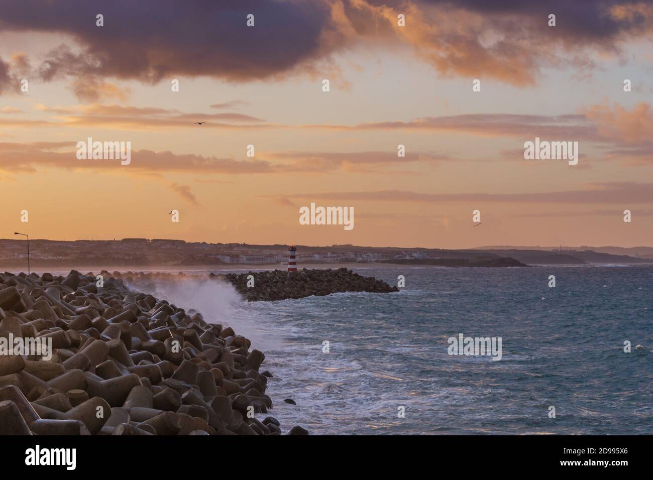 Faro di Peniche con spiaggia di Supertubos sullo sfondo al tramonto con onde che si infrangono, in Portogallo Foto Stock