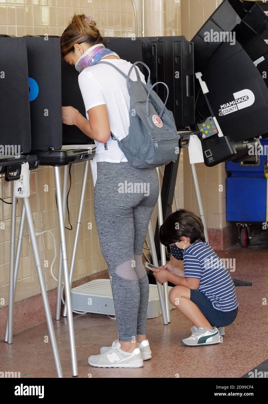 Miami, Stati Uniti. 03 Nov 2020. I residenti della Florida si trovano alla cabina di voto mentre suo figlio gioca con il suo iPhone il giorno delle elezioni per votare alle elezioni presidenziali del 2020 alla stazione dei vigili del fuoco di Miami 2 a Miami, Florida martedì 3 novembre 2020. Le linee dei siti di scrutinio sono più brevi del normale a causa del numero di elettori che hanno votato in anticipo o hanno utilizzato i voti per posta. La distanza sociale è in vigore a causa della pandemia di COVID-19. Foto di Gary i Rothstein/UPI Credit: UPI/Alamy Live News Foto Stock