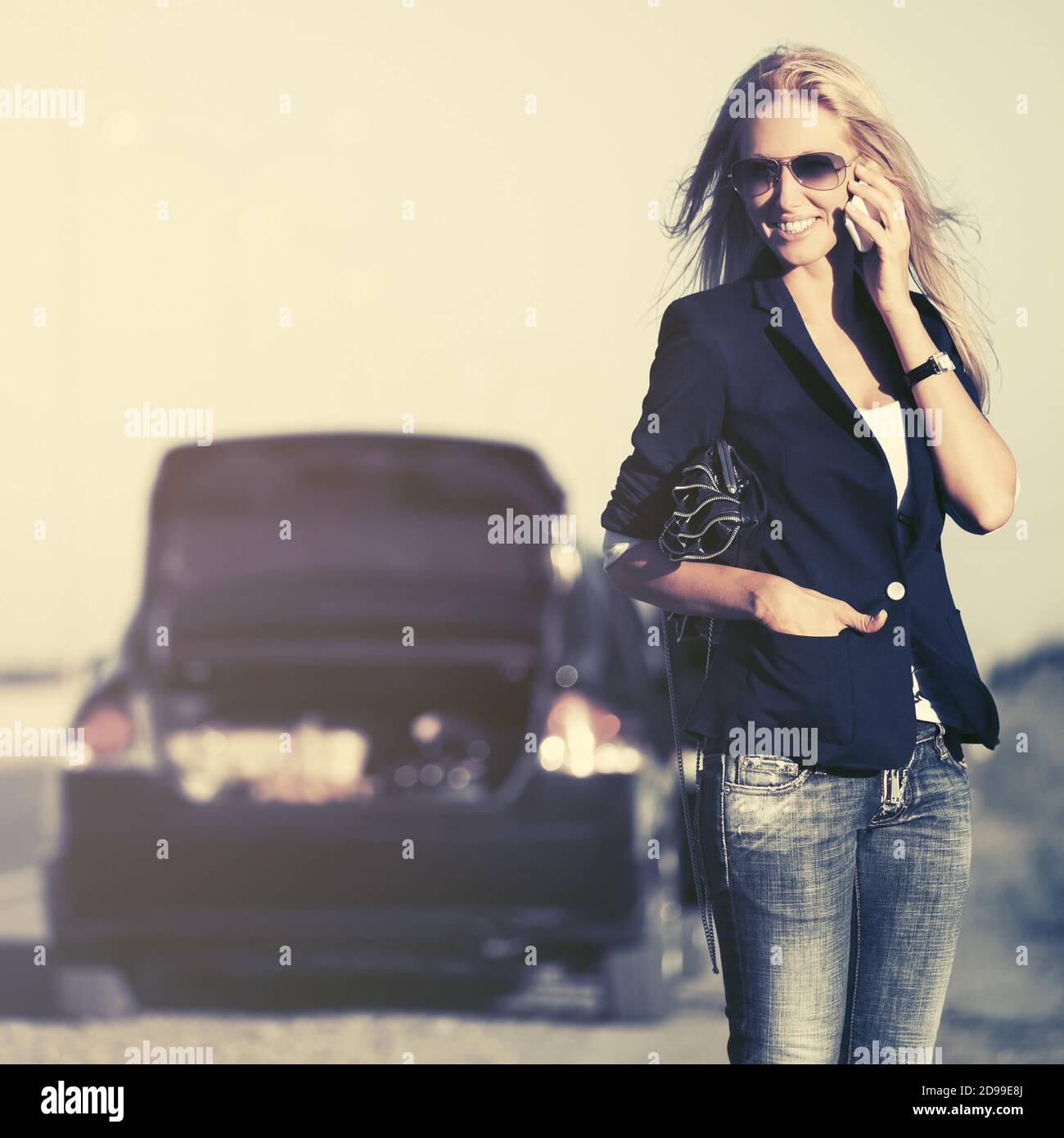 Giovane donna di affari bionda di moda che chiama sul telefono cellulare  successivo A macchina rotto elegante modello femminile in blu scuro blazer  e jeans Foto stock - Alamy